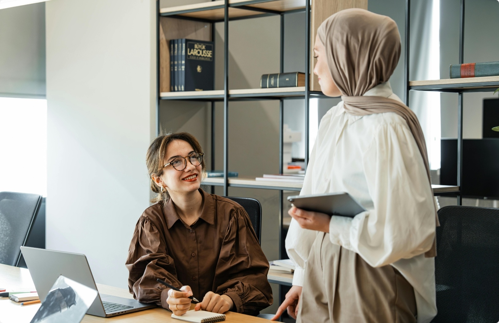 A Muslim woman and an European woman having a talk at their desk in an office