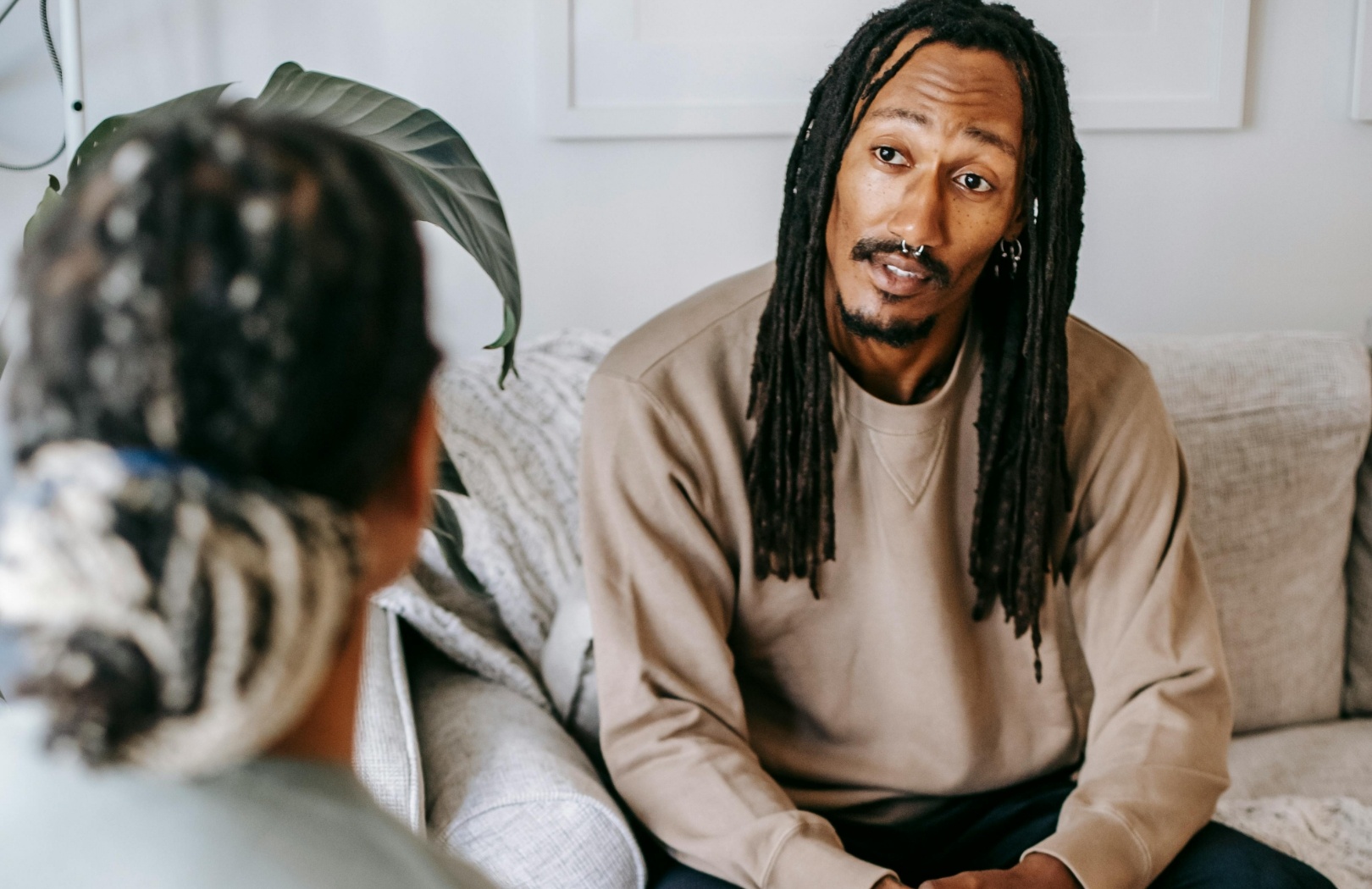 Man with dreadlocks in a conversation, sitting on a sofa