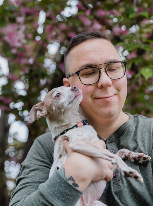 Man with glasses holding a small dog and smiling with his eyes closed