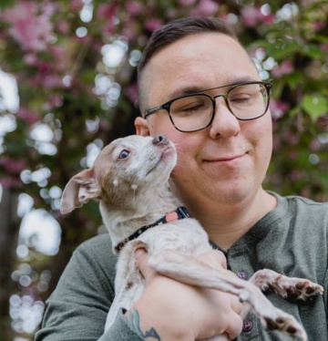 Mann mit Brille hält einen kleinen Hund und lächelt, während er die Augen geschlossen hat